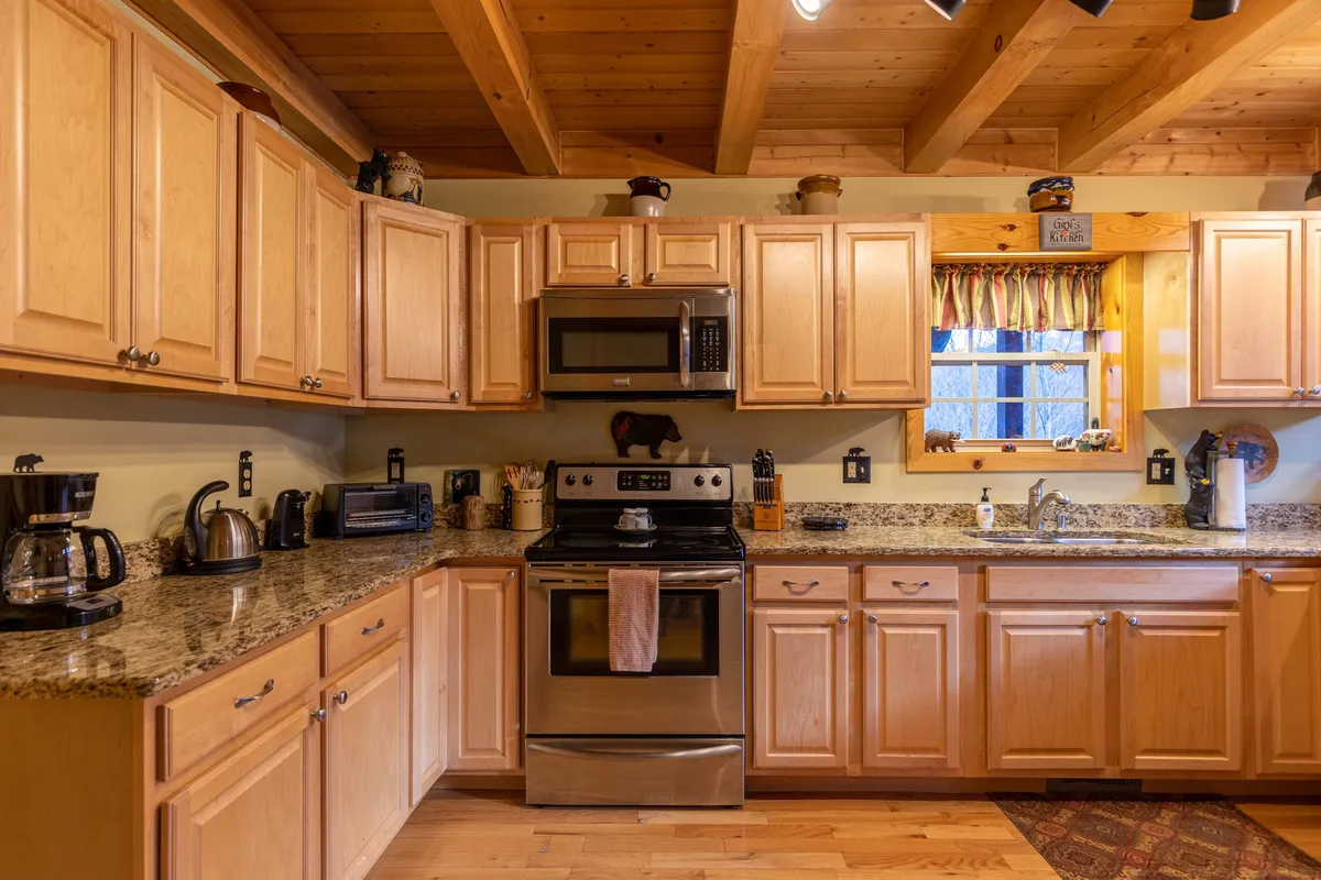 A cozy kitchen space featuring granite countertops, stainless steel appliances, and wooden cabinets. A window with curtains allows warm light to fill the room, creating an inviting atmosphere ideal for gathering, cooking, and sharing meals.