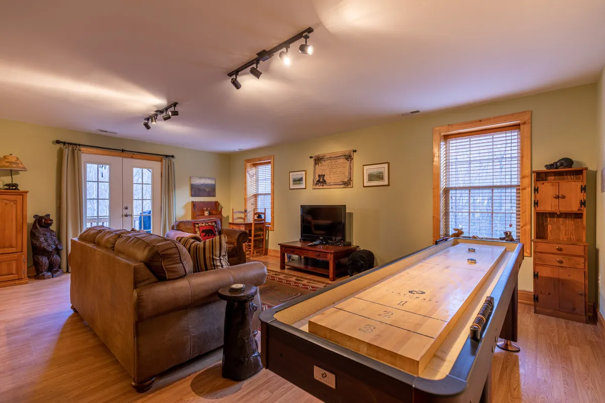 This image shows the heart of the living space, featuring a shuffleboard table, a comfortable sofa, a television, and rustic wooden furniture. The setup exudes a sense of fun and camaraderie, with the shuffleboard table inviting guests to engage in friendly competition while the cozy seating area encourages relaxation and conversation.