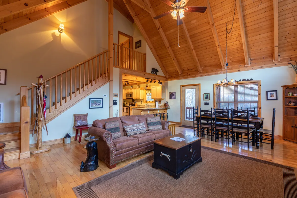 This interior scene highlights a spacious, warm living and dining area with a comfortable sofa, a large dining table, a staircase, and a chandelier overhead—ideal for family gatherings, meals, and movie nights together.