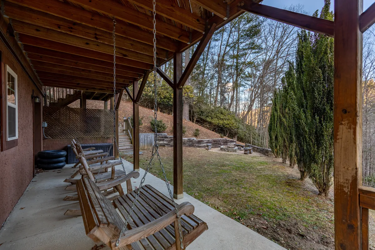 A tranquil outdoor scene featuring wooden swing chairs circling a custom stone fire pit, all nestled among tall trees. The area is clearly designed for gatherings, storytelling, and evenings under the stars.
