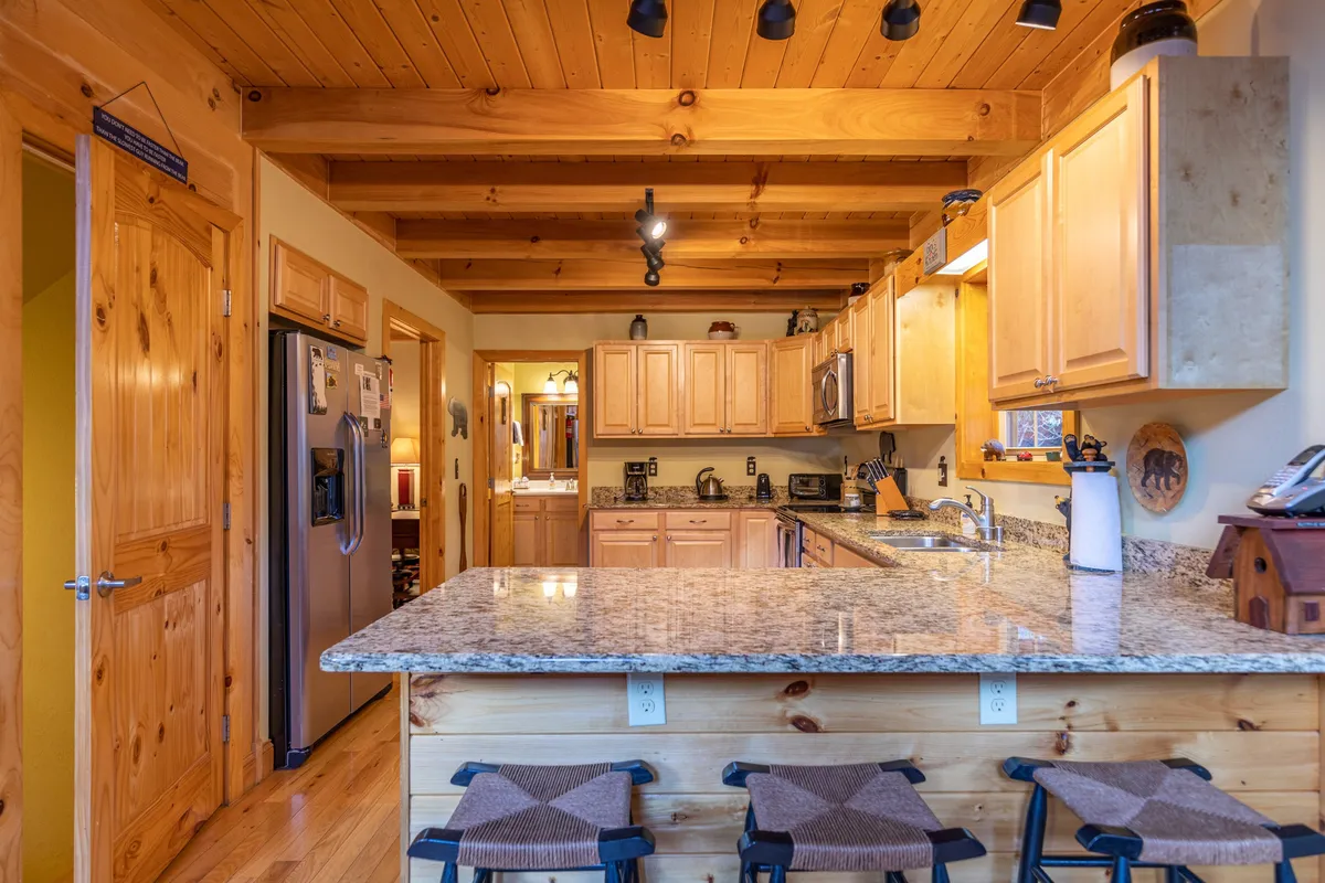 A welcoming kitchen scene, complete with granite countertops, wooden cabinetry, bar stools, and modern appliances. The open layout encourages both culinary creativity and social interaction, making it ideal for group breakfasts or late-night snacks.