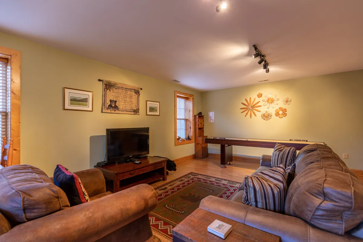 A downstairs den featuring a comfortable sofa, television, decorative wall art, and a cozy rug. The space is ideal for unwinding with family or friends after a day outdoors.