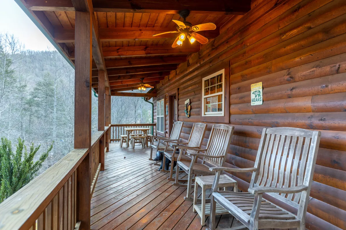 A cozy covered deck with wooden rocking chairs, a table for drinks or games, and a ceiling fan for comfort. The setup invites relaxation, socializing, and enjoying mountain breezes at any time of day.