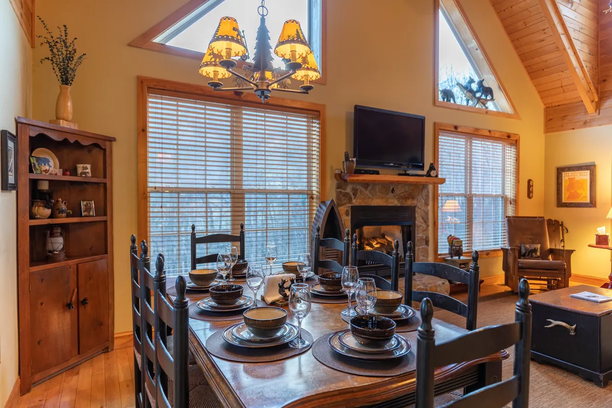 This interior image captures a charming dining table set for a meal, with a warm fireplace glowing in the backdrop and a statement chandelier overhead. The scene conveys a sense of family togetherness and the kind of memorable meals and conversations that define Bear Creek’s main level.